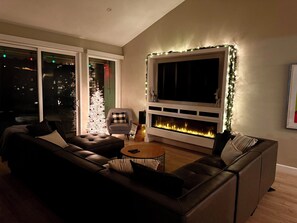 A modern living room with a fireplace, a large window, and a Christmas tree. - 3-Bedroom Condo in Palm Desert – Enjoy Access to Private Golf/Tennis/Pickleball! (Palm Desert)