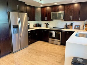 A modern kitchen with dark wooden cabinets, stainless steel appliances, and a white countertop. - 3-Bedroom Condo in Palm Desert – Enjoy Access to Private Golf/Tennis/Pickleball! (Palm Desert)