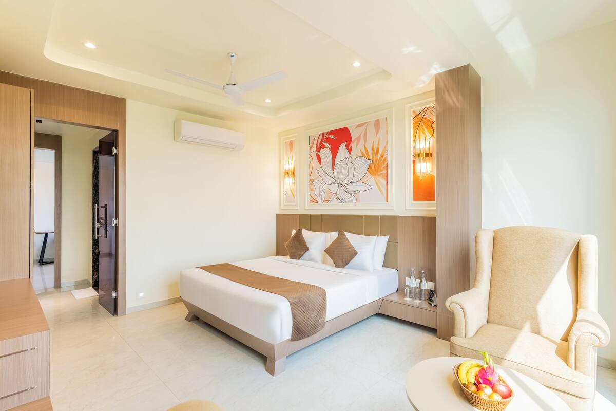 Una habitación de hotel moderna con una cama grande, una zona de estar con una silla y una mesita con fruta.