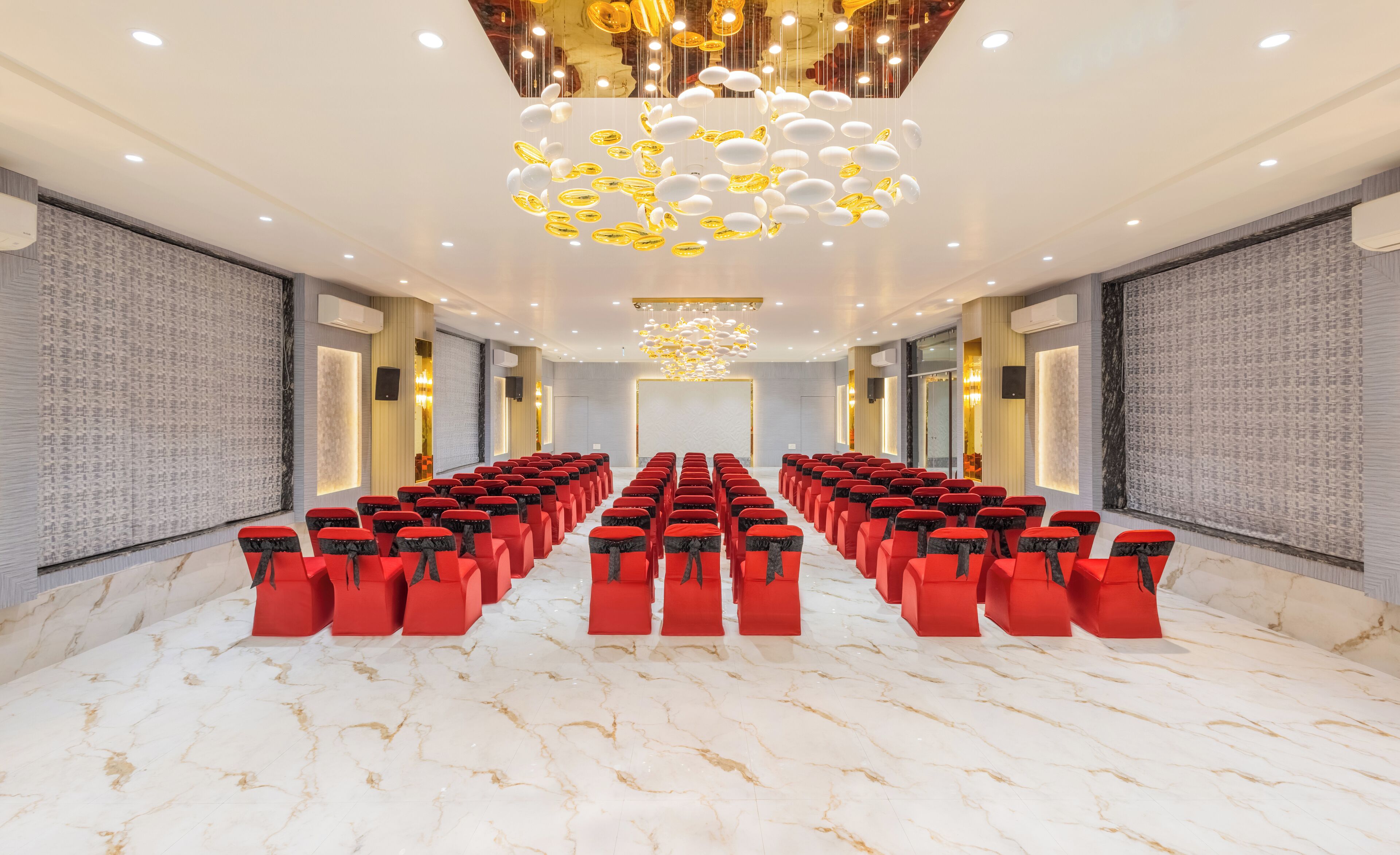 A conference room with rows of red chairs, a marble floor, and a modern chandelier.
