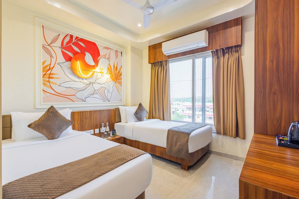 Habitación de hotel con dos camas, un ventanal con cortinas, un equipo de aire acondicionado y una obra de arte colgada en la pared.