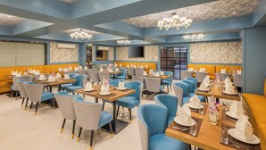 Un restaurant avec des sièges bleus et jaunes, des lustres et des murs à motifs.