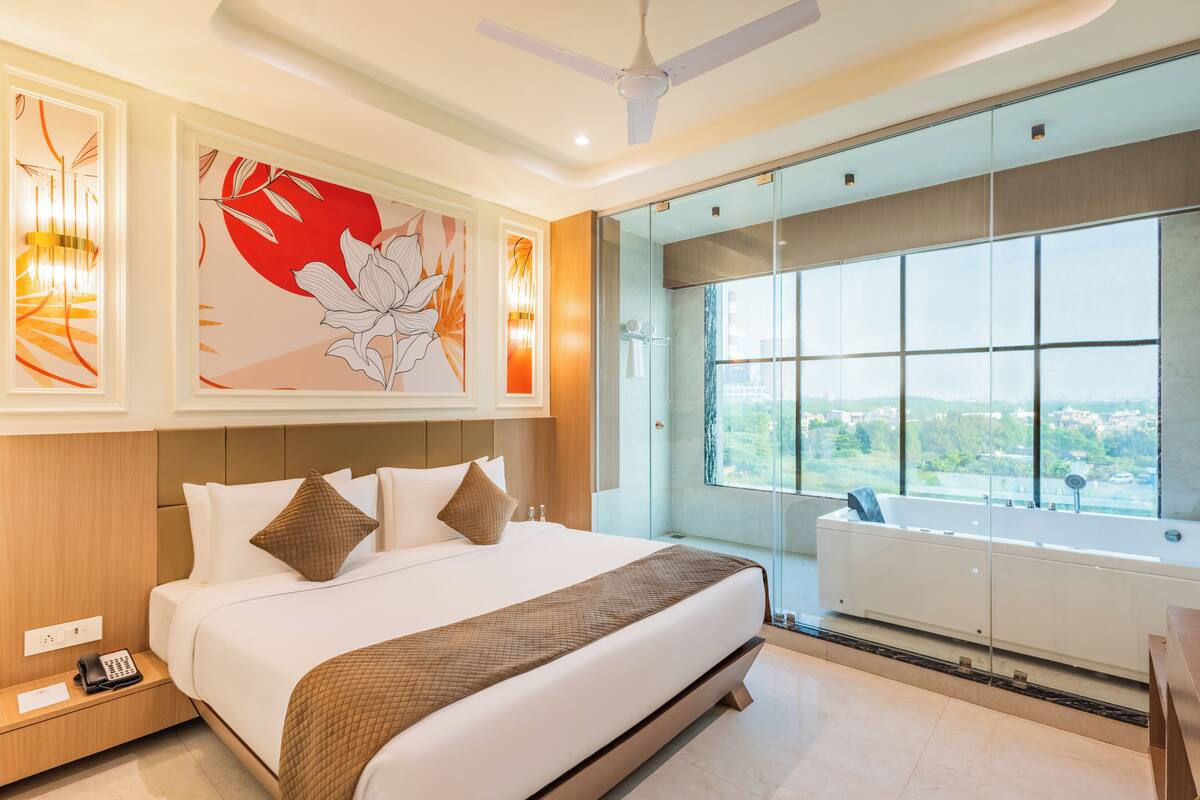 Habitación de hotel moderna con una cama grande, cabina de ducha de vidrio y vistas a la ciudad.