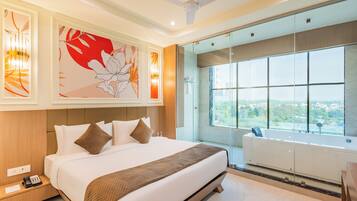 A modern hotel room with a large bed, a glass shower enclosure, and a city view.