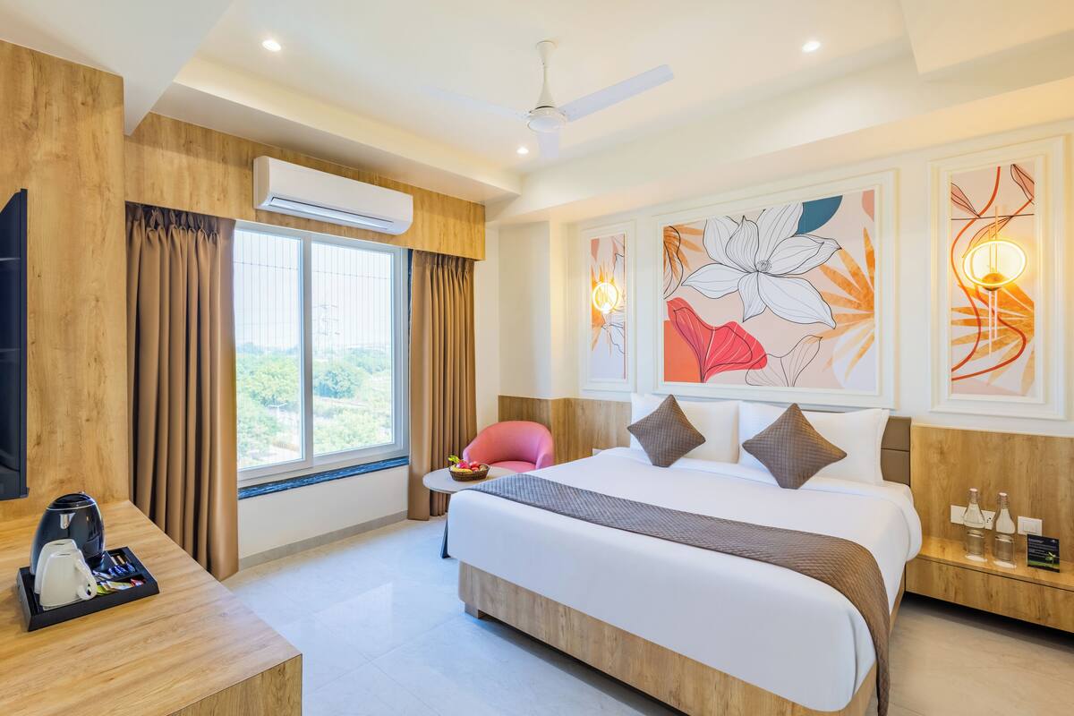 Una habitación de hotel moderna con una cama grande, un escritorio con cafetera, una silla y obras de arte en las paredes.
