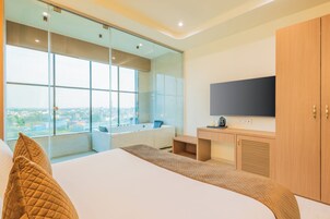 Habitación de hotel moderna con una cama grande, televisión integrada, un ventanal con vista a la ciudad, bañera y armario.