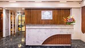 Un comptoir d’accueil d’hôtel avec un revêtement en marbre, un panneau en bois et le logo de « ENRISE by SEMA ».