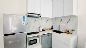 A compact kitchen with a built-in microwave, oven, and dishwasher, white cabinetry, and a marble backsplash. - Loft 360 Apartment (Seminyak)