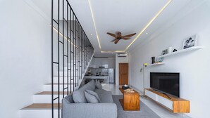 A modern living room with a grey sectional sofa, a wooden coffee table, a flat-screen TV, and a staircase with a metal railing. - Loft 360 Apartment (Seminyak)