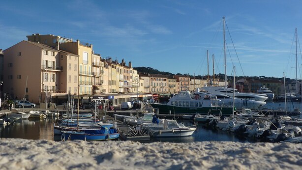 Ein Yachthafen mit vertäuten Booten, ein Sandstrand und Gebäude im Hintergrund.