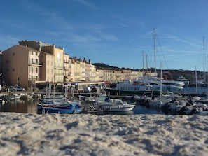 Un puerto deportivo con barcos amarrados, una playa de arena y edificios al fondo.