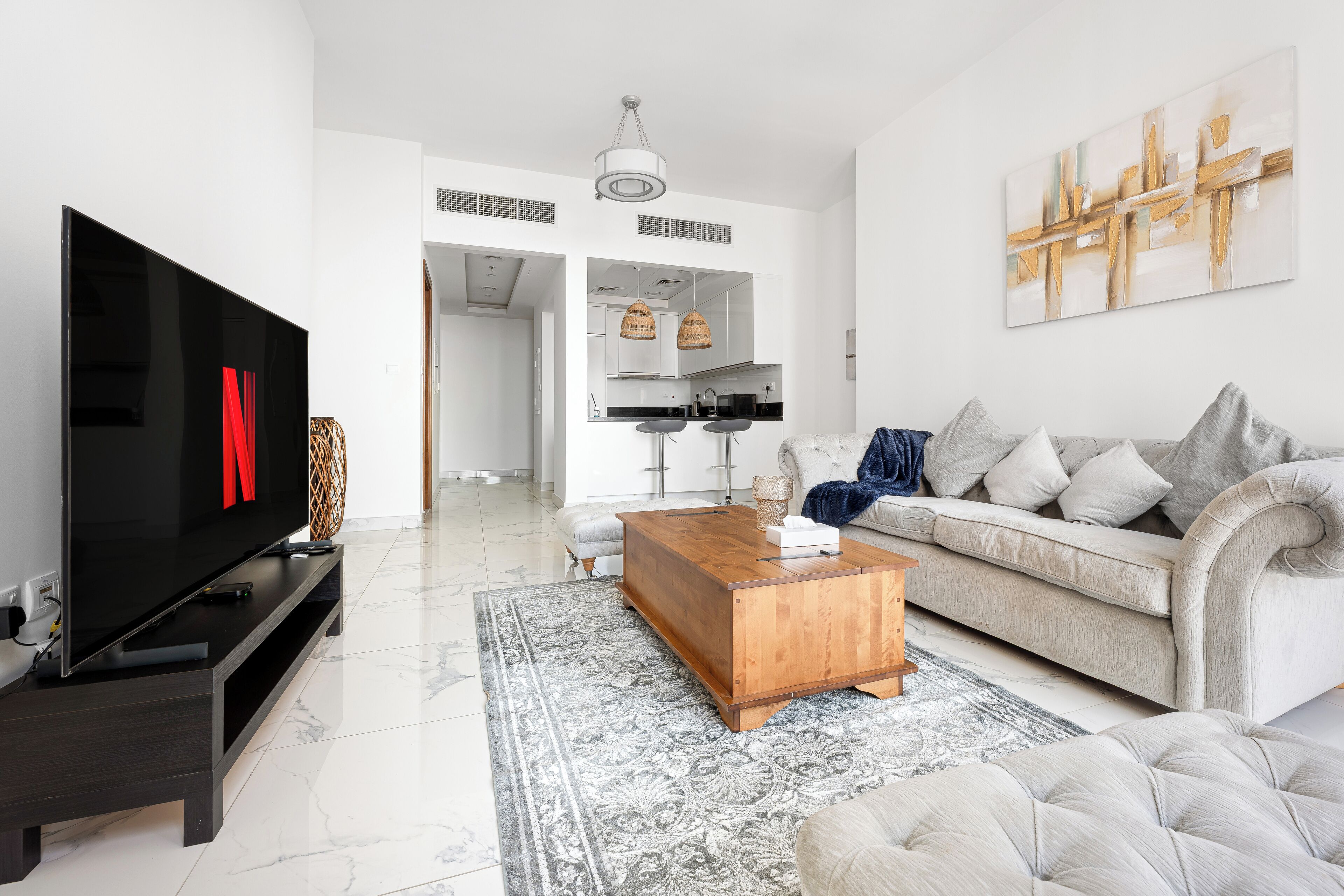A modern living room with a flat-screen TV, a wooden coffee table, a grey sofa, and a patterned rug.
