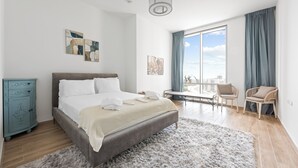 A modern bedroom with a large bed, a dresser, and a view of the city through a large window. - Luxury Leisure Massive Pool Oasis (Dubai)