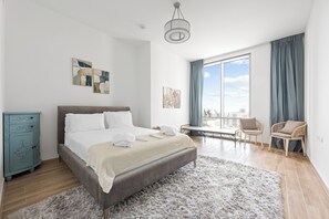 Ein modernes Schlafzimmer mit einem großen Bett, einer Kommode und Blick auf die Stadt durch ein großes Fenster.