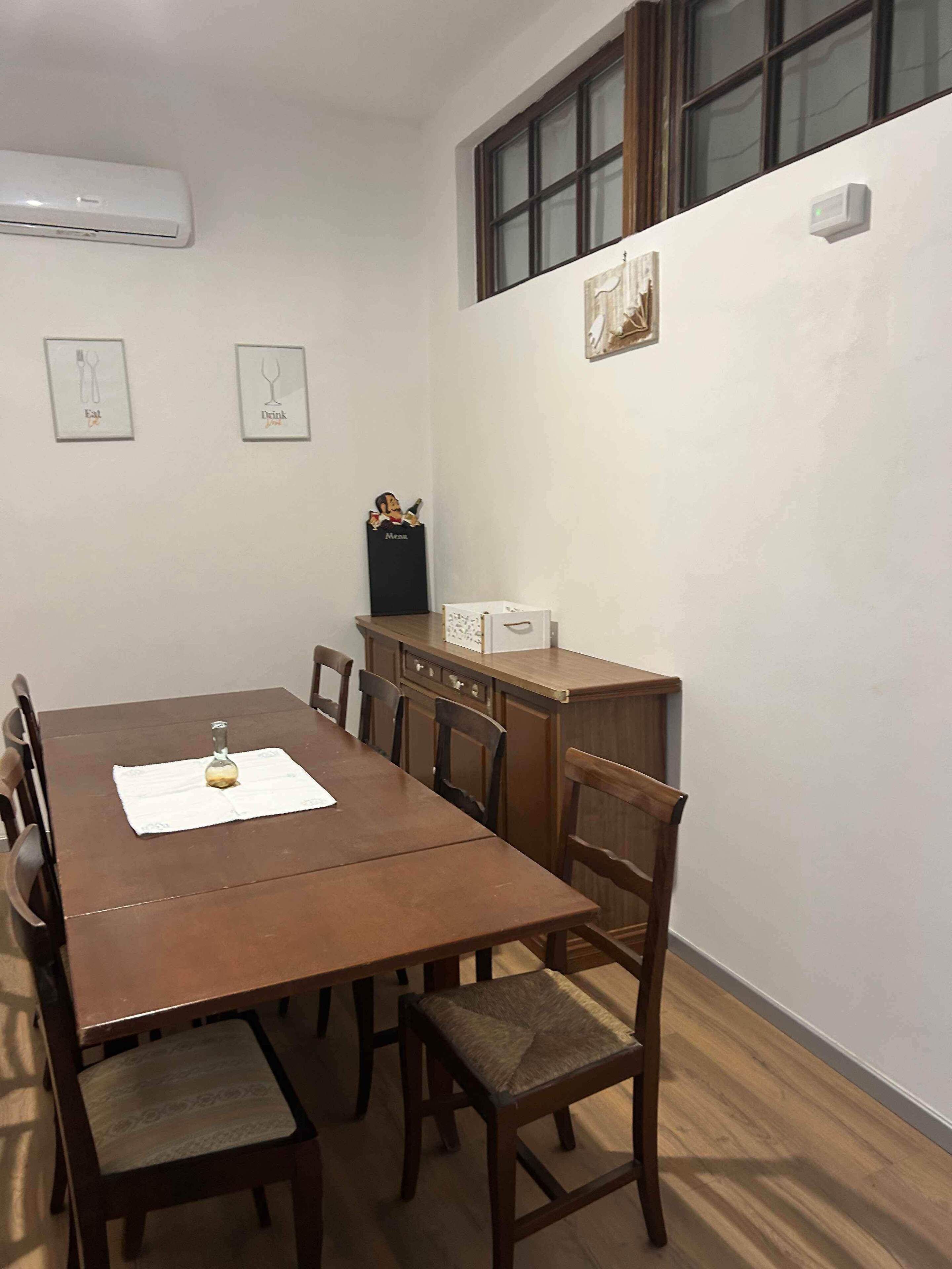 Un comedor con mesa y sillas de madera, una ventana con persianas y aire acondicionado instalado en la pared.