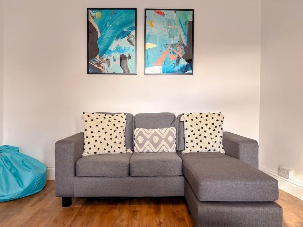 Ein graues Ecksofa mit gemusterten Kissen, ein blauer Sitzsack und ein abstraktes Kunstwerk an der Wand.