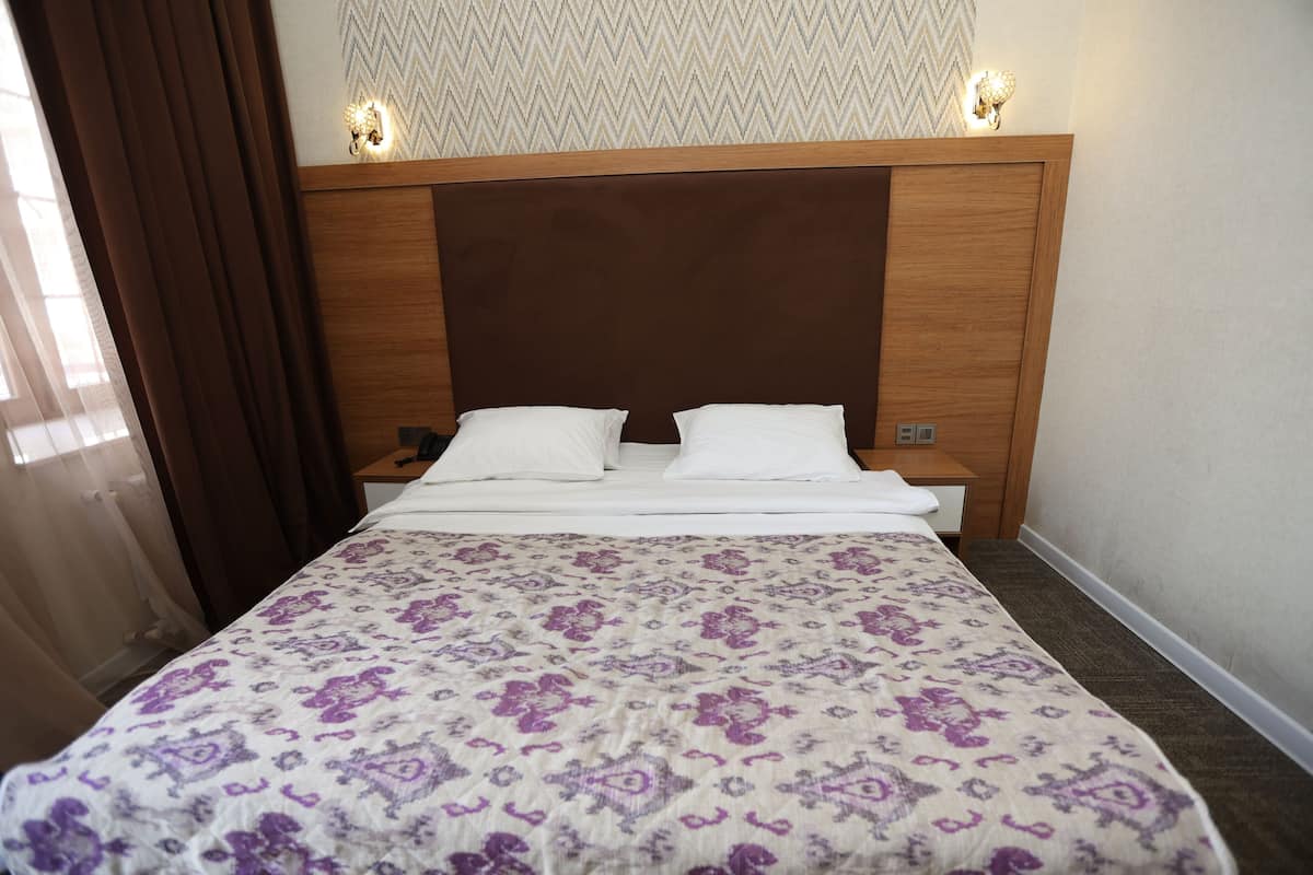 A hotel room with a bed, a nightstand, a lamp, and a window with curtains.