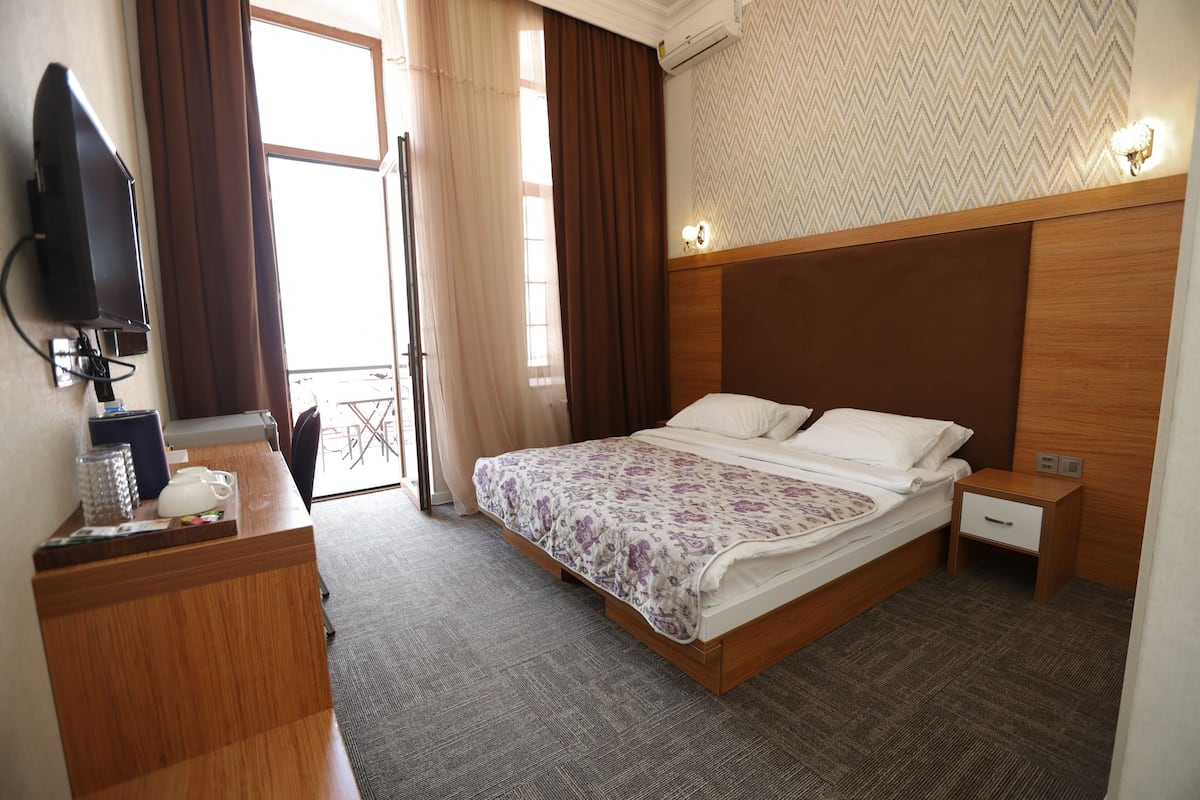 A hotel room with a bed, bedside tables, a desk with a television, and a window with curtains.