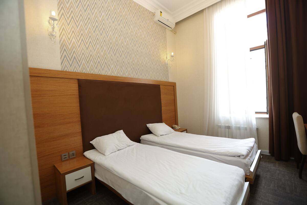 A hotel room with two single beds, a wooden headboard, a nightstand with a phone, and a patterned wallpaper.