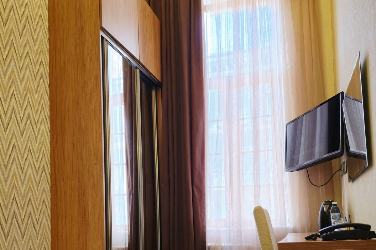 A hotel room with a bed, a desk with a television, a chair, and a window with curtains.