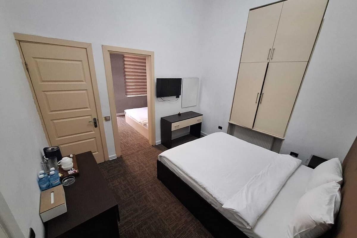 A hotel room with a bed, a desk with a chair, a TV, and a wardrobe.