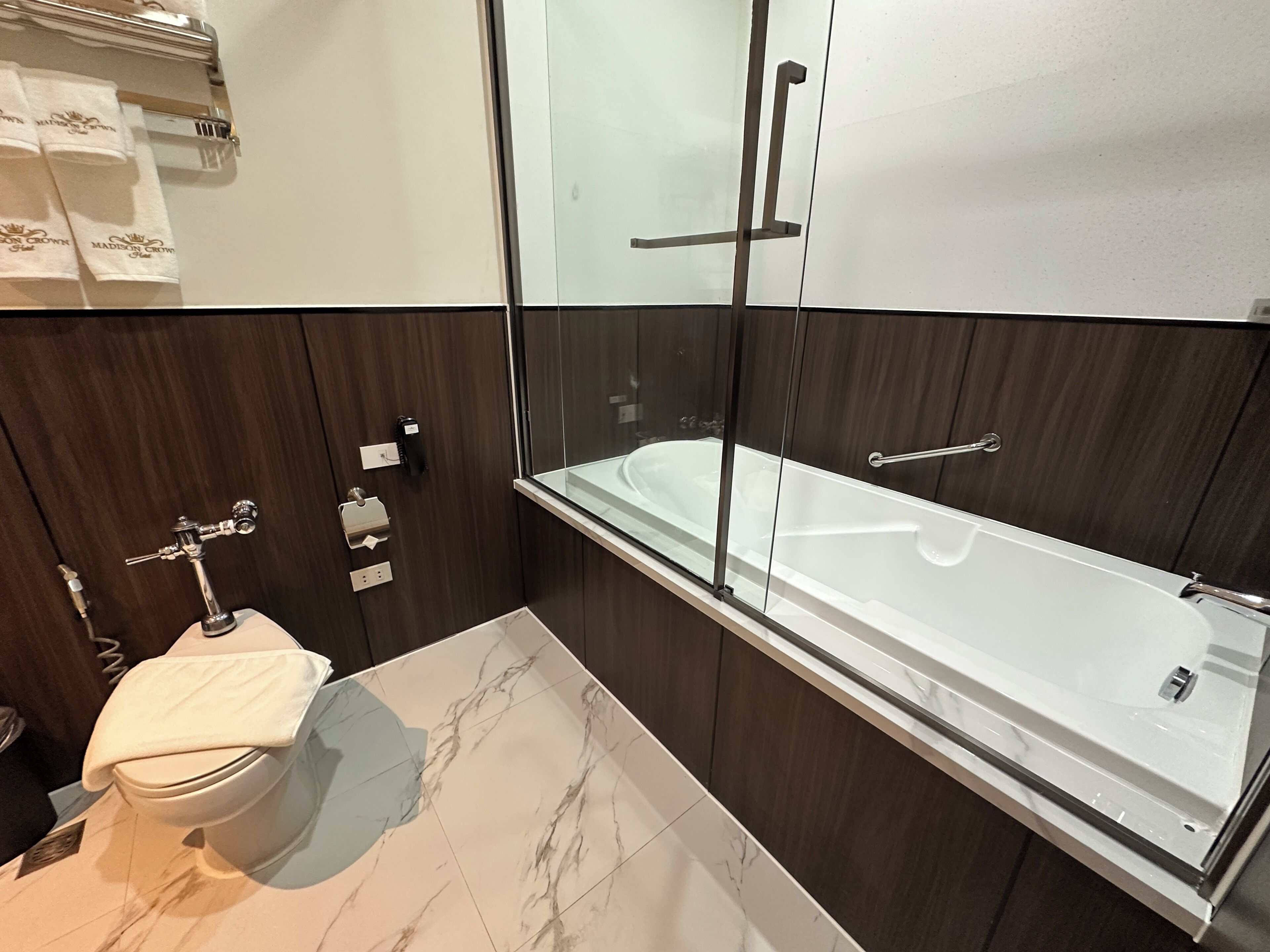 A modern bathroom with a glass-enclosed bathtub, a toilet, and a vanity with a towel rack.
