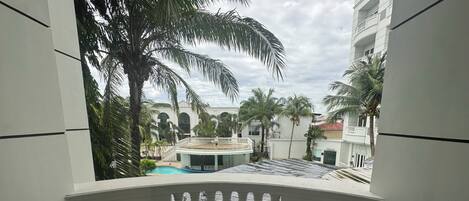A balcony with a view of a pool, palm trees, and a building with arched windows.