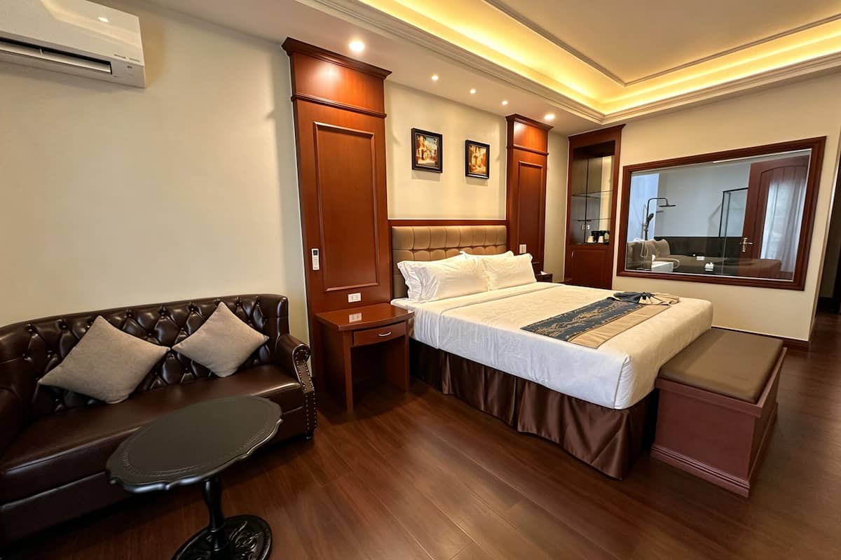 A hotel room with a bed, a sofa, a small table, a mirror, and a wardrobe.