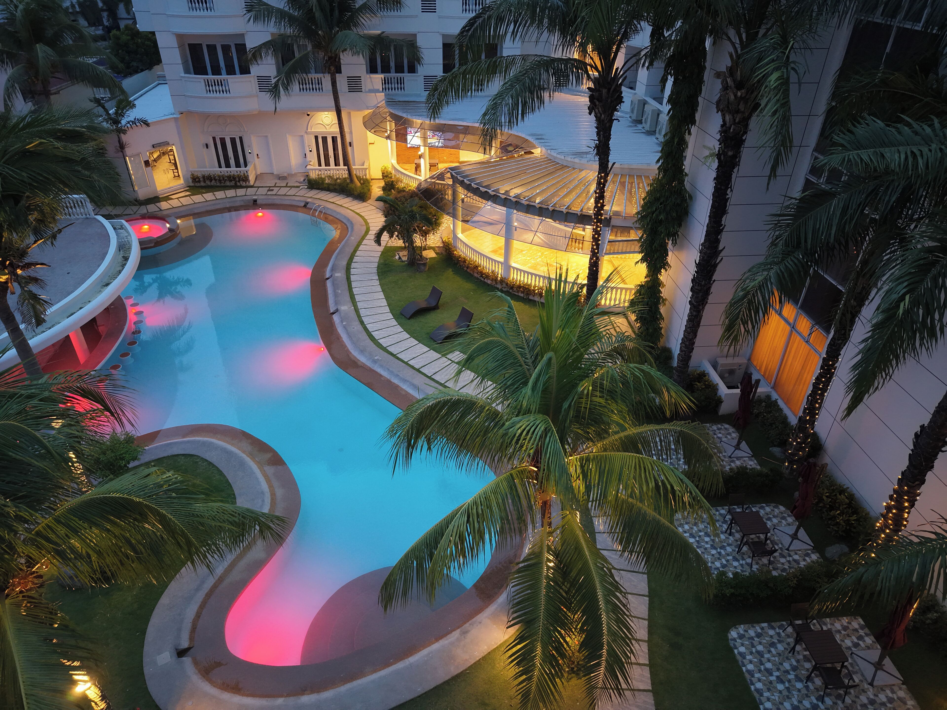 A swimming pool with a curved design, surrounded by palm trees and a building with balconies.