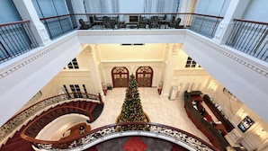 A grand hotel lobby with a central staircase, a Christmas tree, and a reception desk.