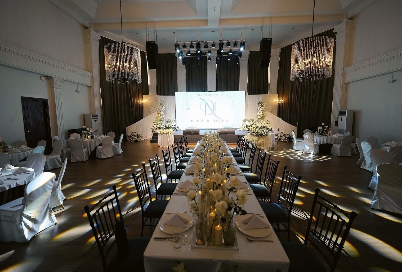 Un salón de banquetes con una larga mesa dispuesta para una boda, candelabros y una pantalla de proyección.