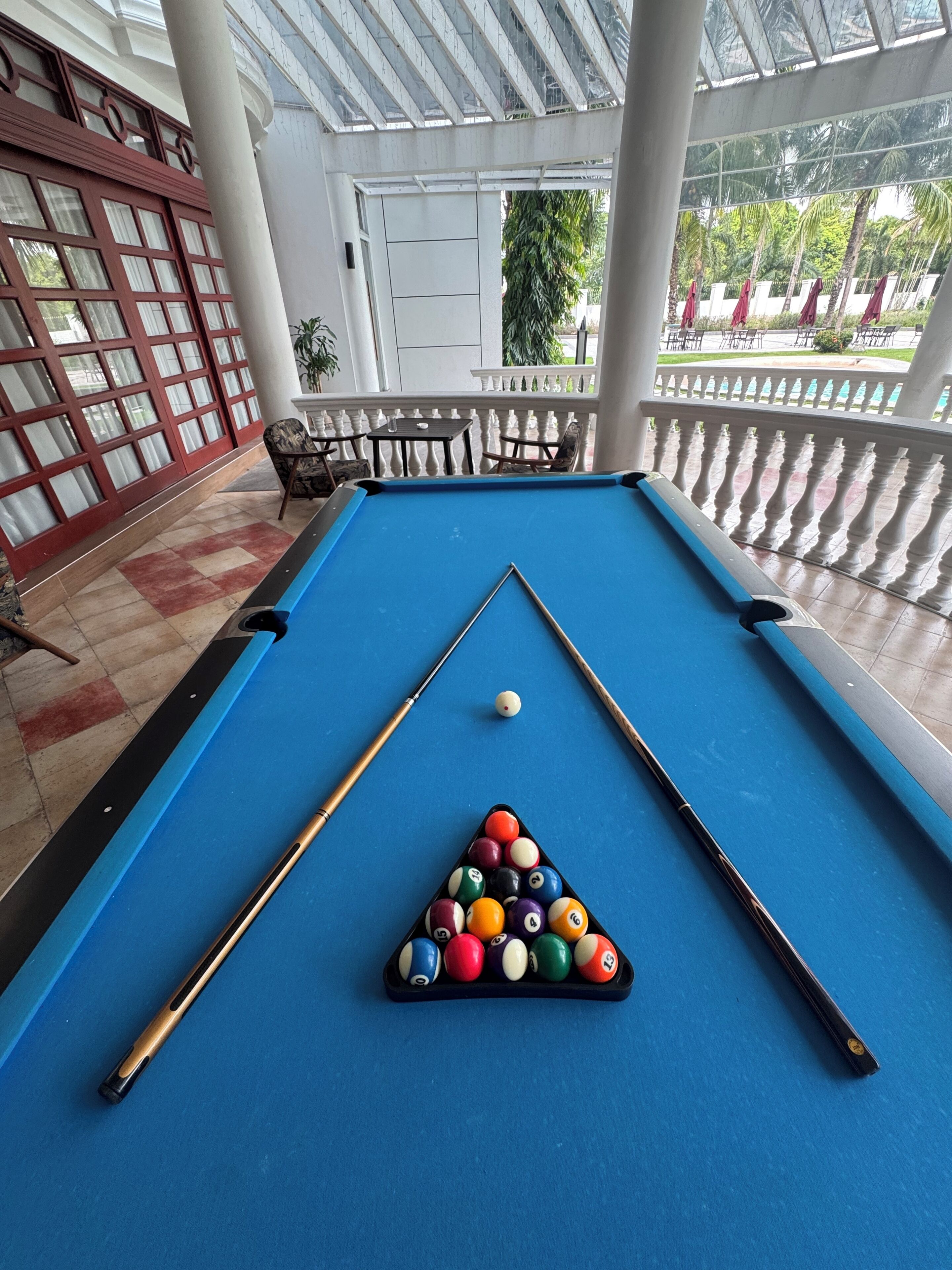 A pool table with a triangular rack of billiard balls, a pool cue, and a table tennis paddle.