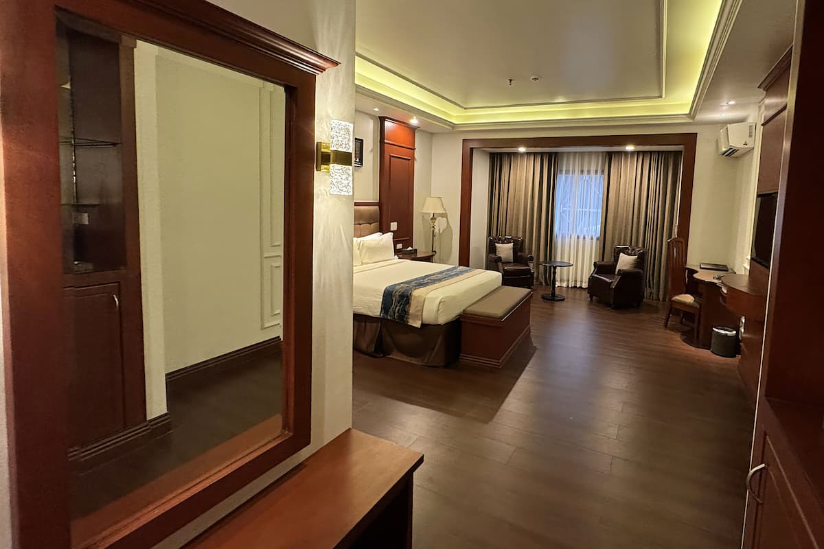 A hotel room with a bed, a desk, a chair, a small table, and a mirror.