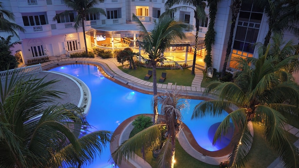 A swimming pool with a curved design, surrounded by palm trees and a building with balconies.
