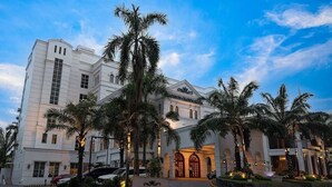 A large, white hotel with a grand entrance, palm trees, and a clear sky.