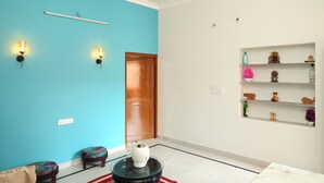 Una habitación con una pared azul, una puerta de madera, un estante blanco con adornos y una pequeña mesa redonda con un florero.