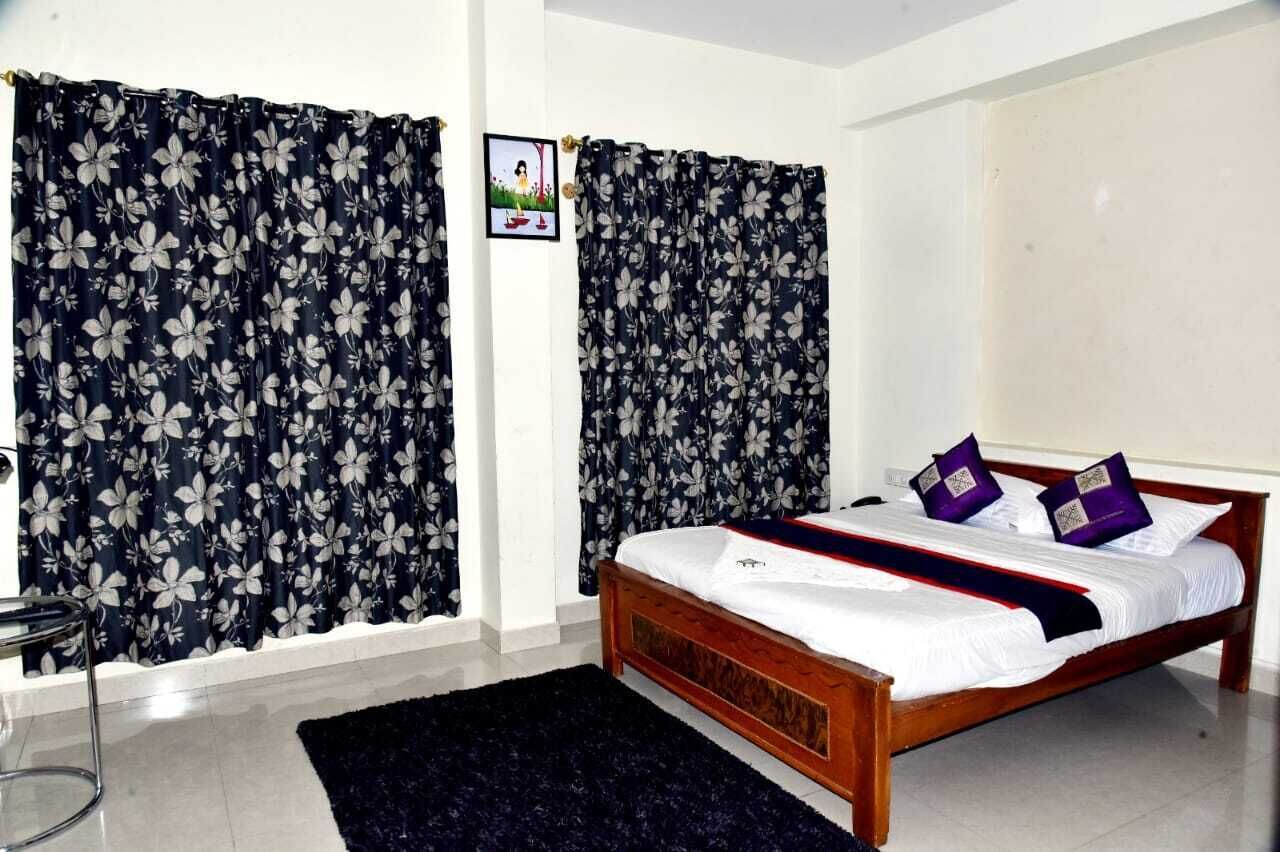 Une chambre à coucher avec un lit en bois, des rideaux foncés à motifs floraux, une petite table de chevet et un tapis sombre.