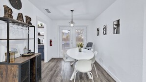 Une cuisine moderne avec un plan de travail blanc, un coin bar en bois avec des verres et une table de salle à manger ronde avec des chaises.