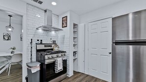 Una cocina moderna con armarios blancos, un refrigerador de acero inoxidable, una estufa a gas y un cubo de basura.