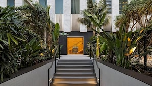 A modern staircase with a glass elevator door at the top, surrounded by lush greenery. - Cozy Room in DTLA w/ Restaurant & Chic Lounge Spot (Los Angeles)