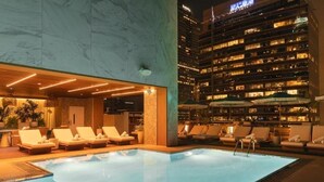 An indoor swimming pool with lounge chairs and a view of a high-rise building at night. - Cozy Room in DTLA w/ Restaurant & Chic Lounge Spot (Los Angeles)