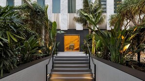 A modern staircase with a glass elevator door at the top, surrounded by lush greenery. - Pet Friendly & Best Value Stay In Premium Suite (Los Angeles)
