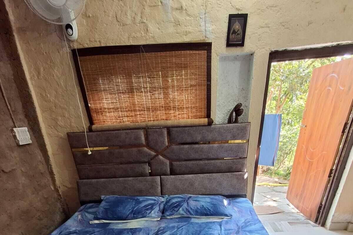 A bedroom with a bed, a headboard, a window with blinds, and a door leading outside.