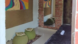 A room with a bed, a large mirror reflecting a colorful painting, and a brick wall. - Junegiri Farms & Homestay (Rishikesh)