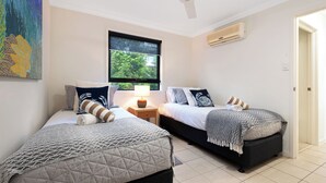 Ein Schlafzimmer mit zwei Betten, einem Deckenventilator, einem Fenster mit Blick auf Grünflächen und einer Klimaanlage.