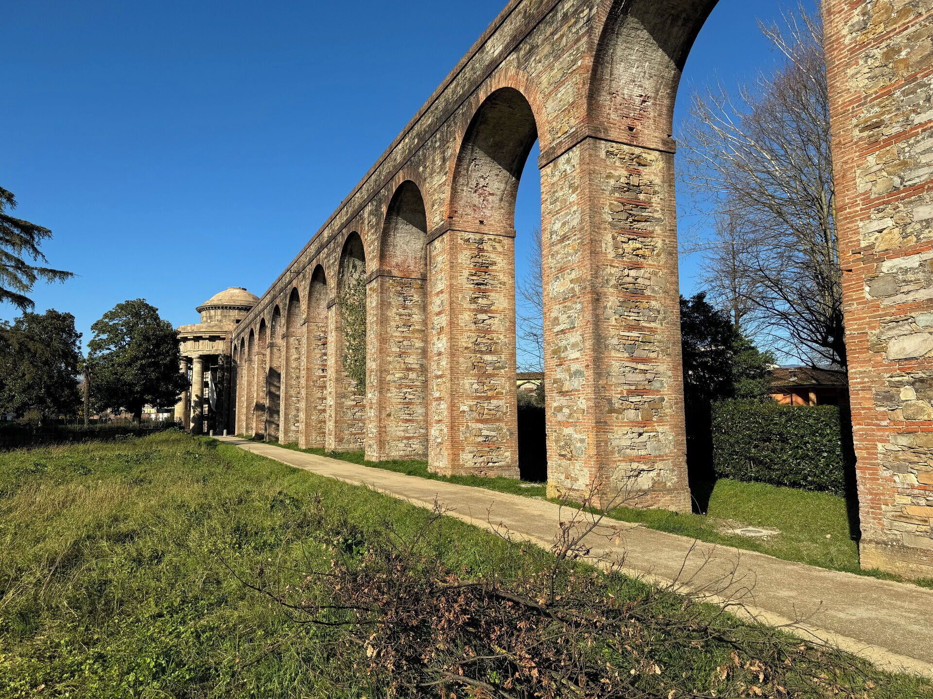 Uma ponte de pedra histórica com arcos e uma estrutura em forma de cúpula ao fundo.