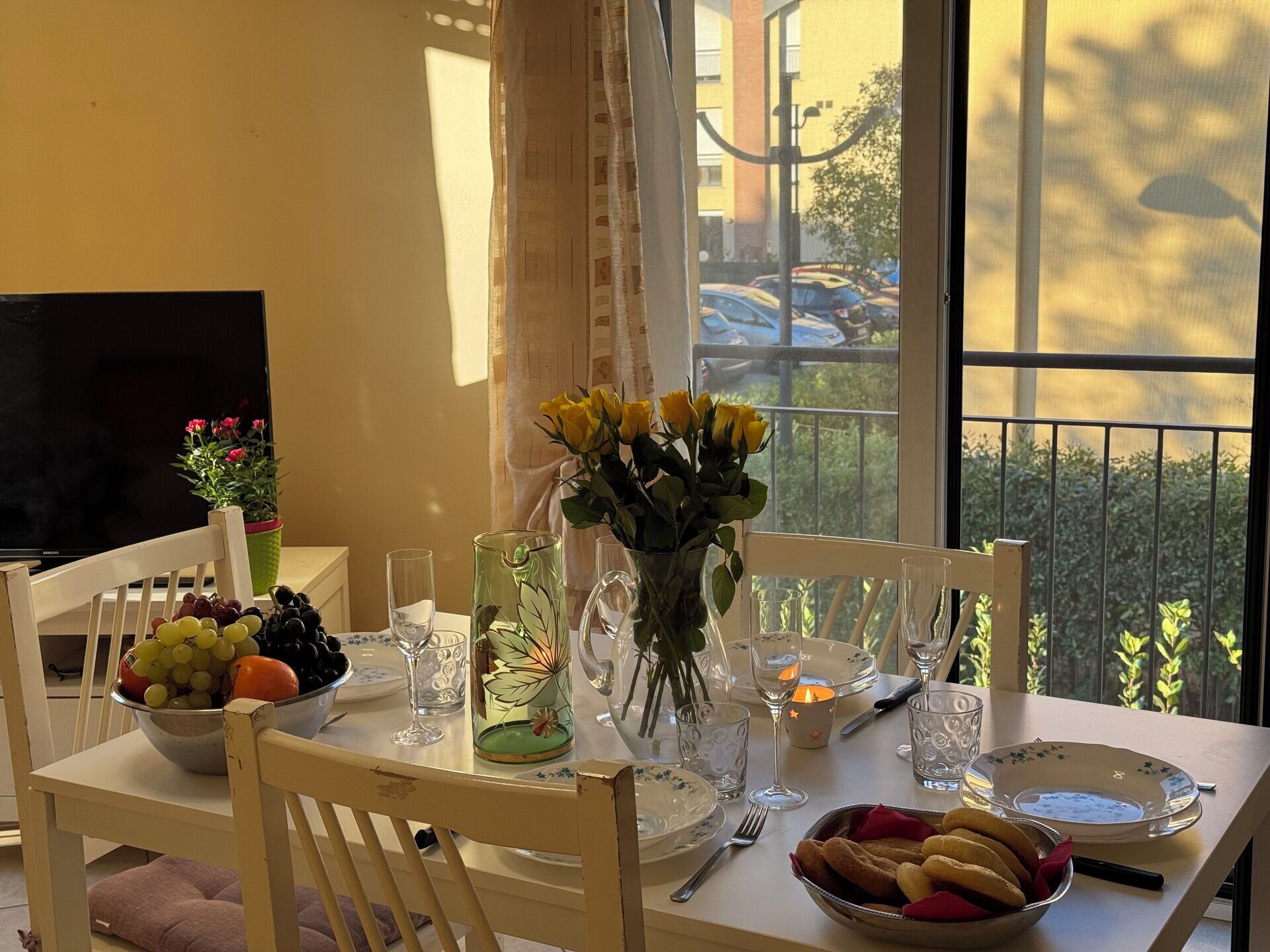 Une table à manger dressée avec un saladier de fruits, un vase de roses jaunes et une bougie.