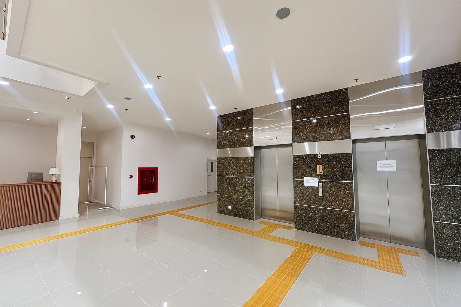 A modern lobby with a reception desk, elevators, and tactile paving for the visually impaired.