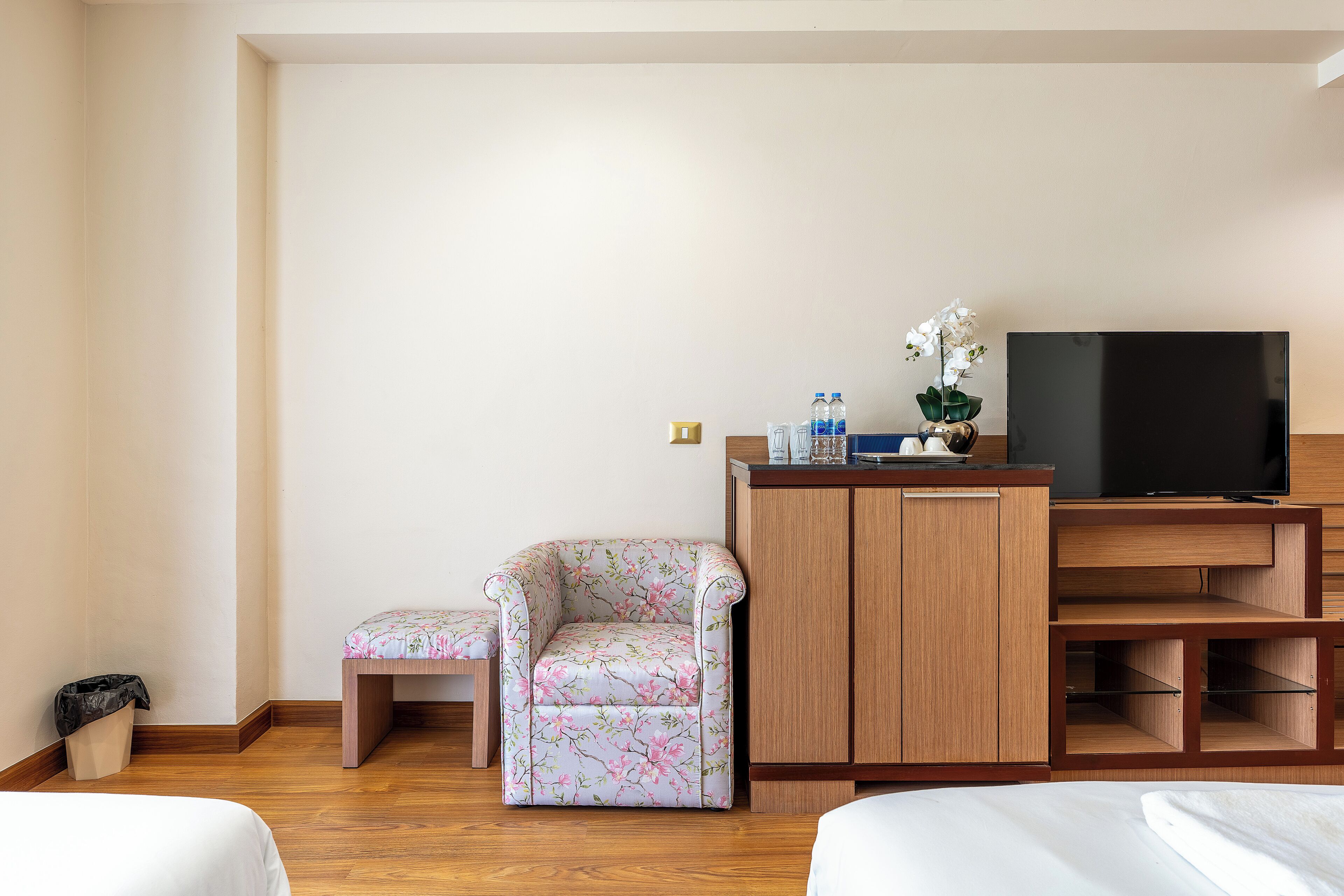 Una habitación de hotel con un armario de madera, un televisor, un sillón floral y una pequeña mesa.