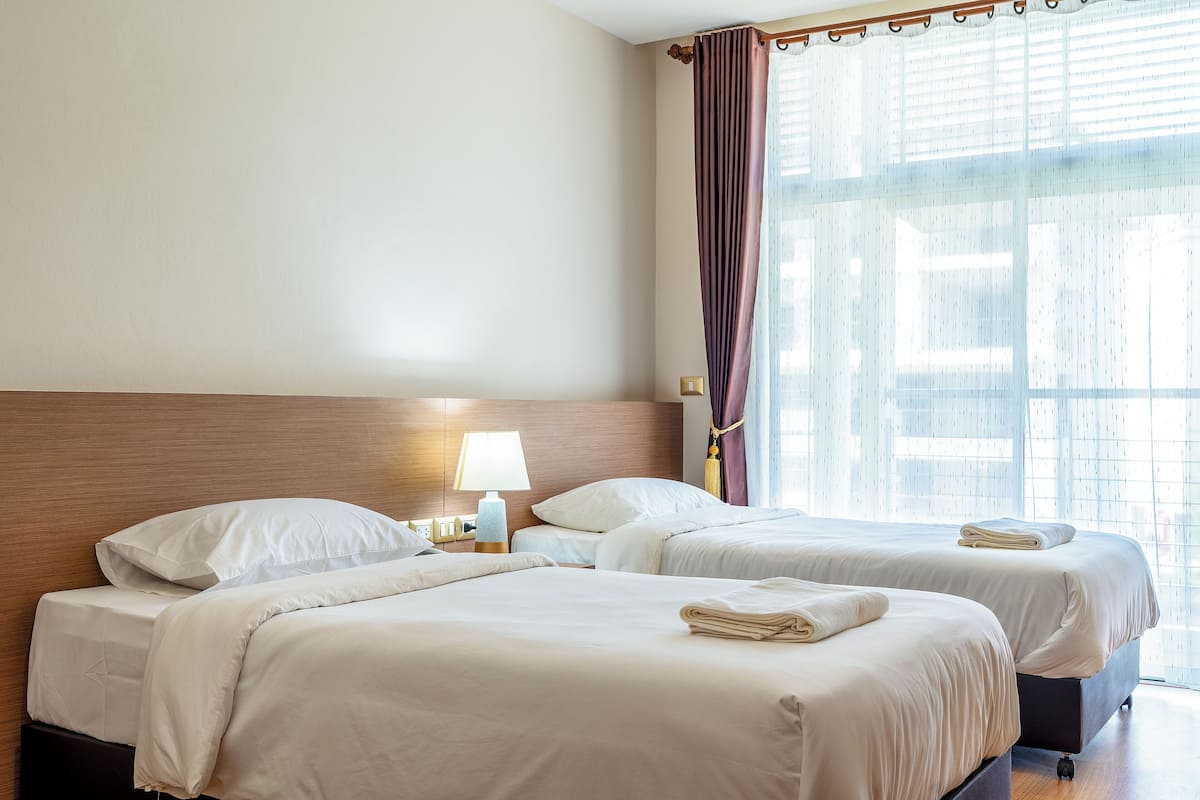 Een hotelkamer met twee bedden, een nachtkastje met een lamp en een raam met gordijnen.